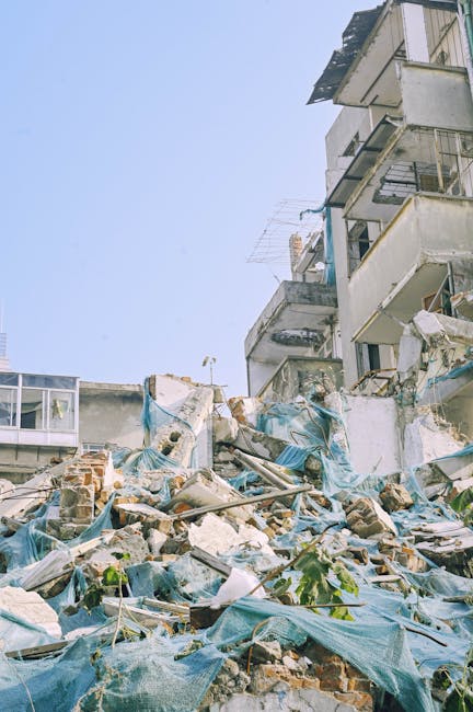 A pile of mixed construction debris and household waste is situated at the base of a multi-storey residential building, with rubble including bricks, broken concrete, and scraps of metal scattered acr